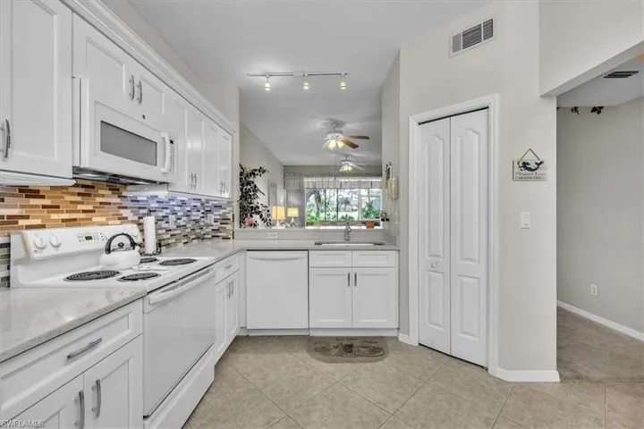 Kitchen featuring white appliances, white cabinets, light tile patterned floors, decorative backsplash, and ceiling fan