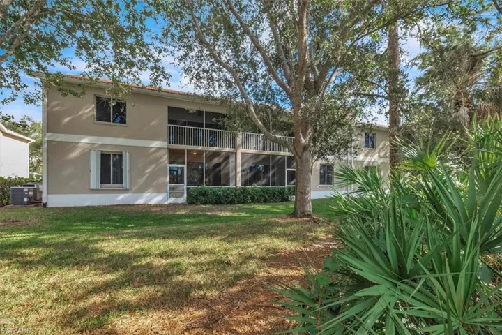 Back of property with a sunroom, stucco siding, a balcony, and a lawn