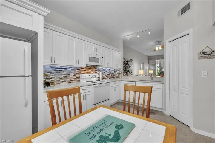 Kitchen with white cabinetry, white appliances, light tile patterned floors, ceiling fan, and backsplash