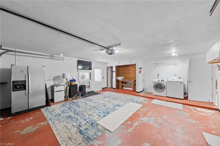 Garage featuring stainless steel fridge with ice dispenser, white fridge, washing machine and dryer, and a garage door opener