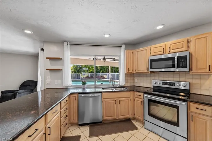Kitchen featuring stainless steel appliances, dark stone counters, light wood finish cabinetry, light tile patterned floors, and open shelves