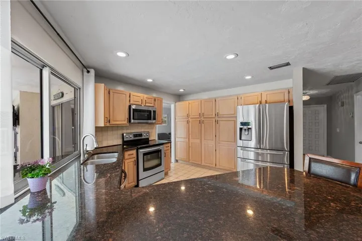 Kitchen featuring dark stone countertops, stainless steel appliances, light wood finish cabinetry, decorative backsplash, and recessed lighting