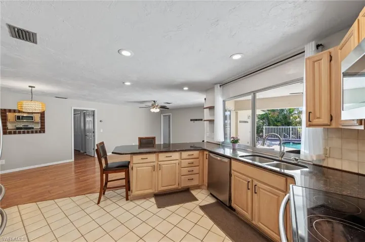 Kitchen with light wood finish cabinetry, stainless steel appliances, a peninsula, and light tile patterned flooring