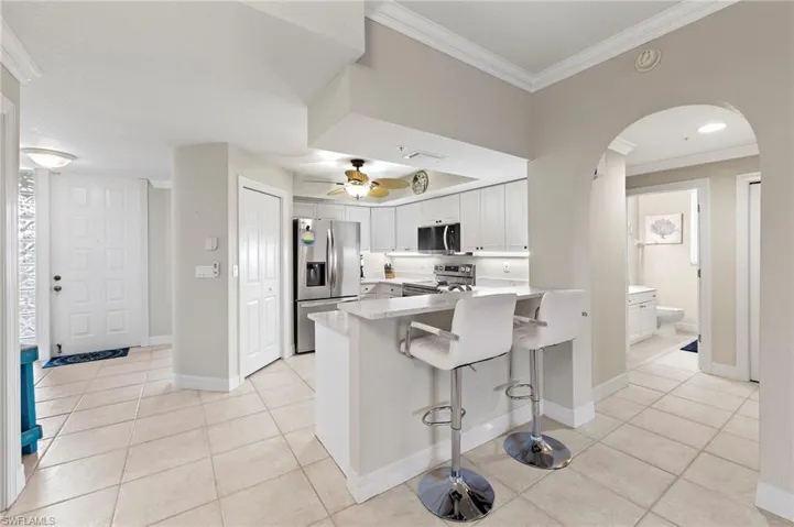 Kitchen with appliances with stainless steel finishes, kitchen peninsula, a kitchen bar, ceiling fan, and light tile floors
