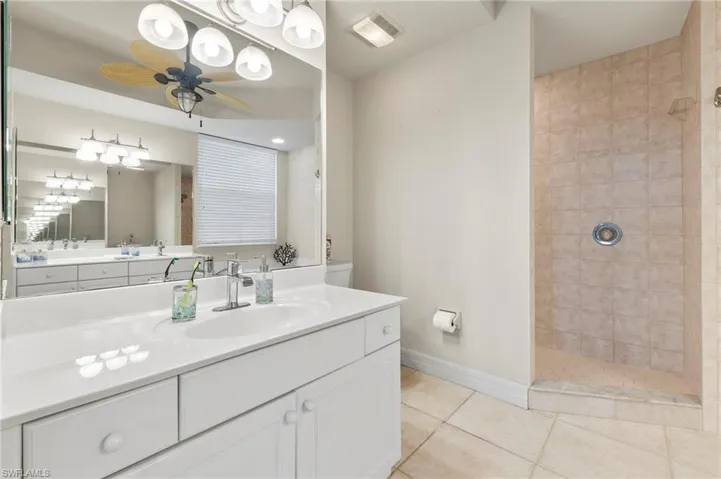 Bathroom with a tile shower, tile flooring, vanity, and ceiling fan