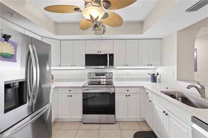 Kitchen featuring stainless steel appliances, a tray ceiling, white cabinetry, sink, and light tile floors
