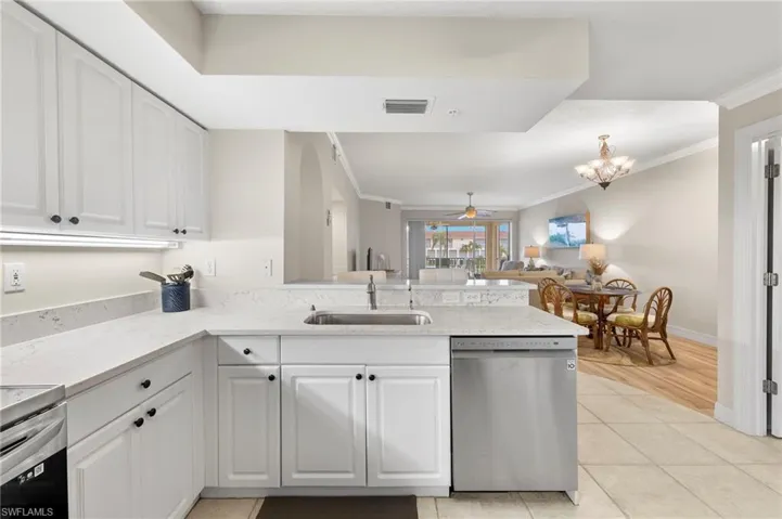 Kitchen featuring crown molding, stainless steel dishwasher, ceiling fan with notable chandelier, light tile floors, and white cabinets