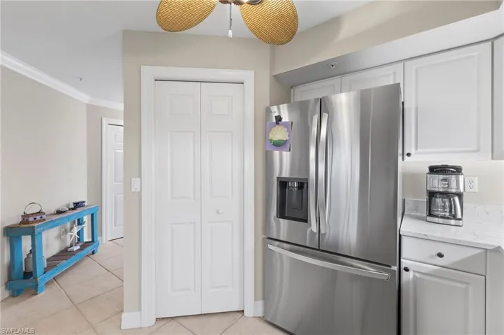 Kitchen featuring light stone counters, ceiling fan, crown molding, stainless steel fridge, and light tile floors