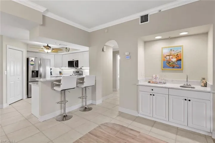 Kitchen featuring ceiling fan, stainless steel appliances, light tile floors, a breakfast bar, and white cabinets