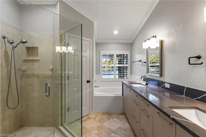 Full bathroom featuring a shower stall, a bath, double vanity, and ornamental molding