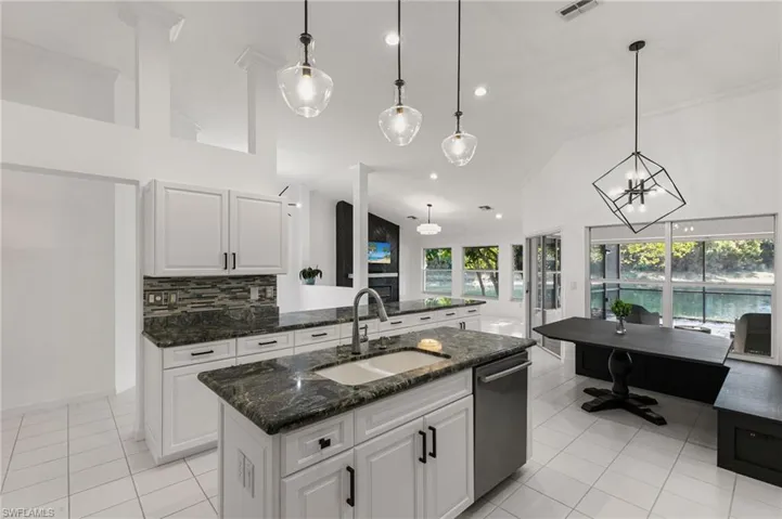 Kitchen with white cabinetry, dark stone counters, an island with sink, light tile patterned flooring, and lofted ceiling