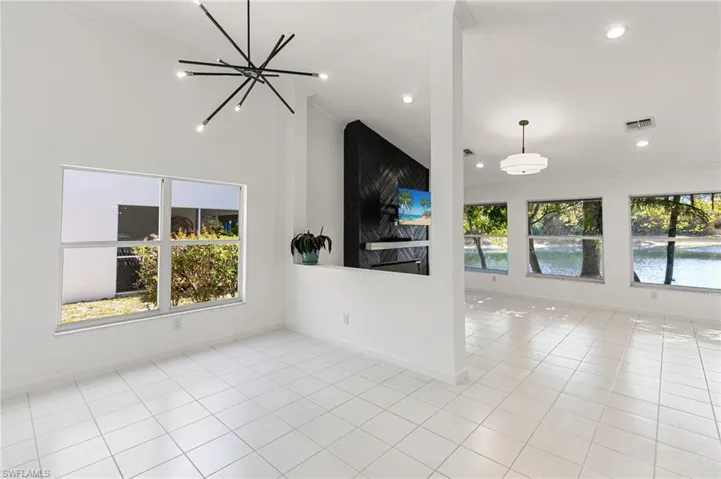 Unfurnished living room with a chandelier, light tile patterned floors, ornamental molding, and lofted ceiling