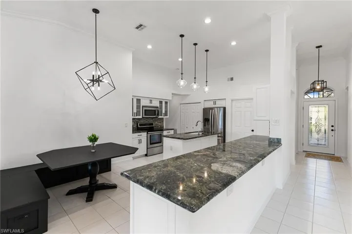 Kitchen featuring suspended lighting, stainless steel appliances, glass insert cabinets, dark stone countertops, and an island with sink