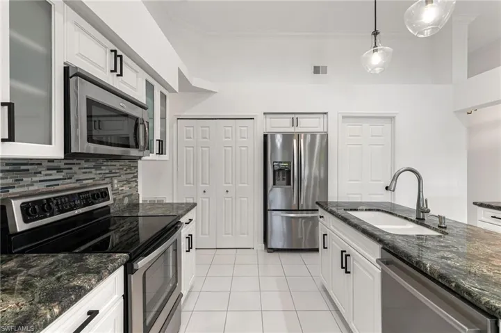 Kitchen featuring stainless steel appliances, dark stone counters, decorative light fixtures, white cabinets, and ornamental molding