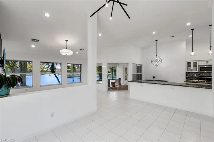 Kitchen with vaulted ceiling, dark stone countertops, glass insert cabinets, hanging light fixtures, and light tile patterned floors