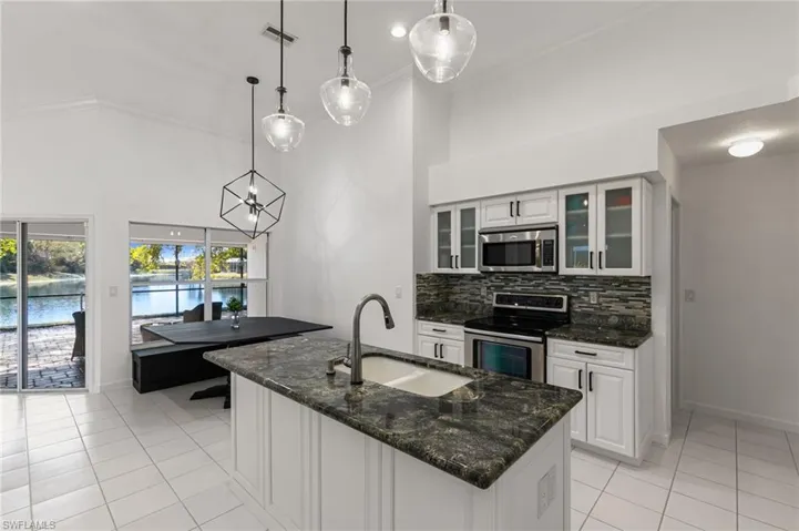 Kitchen featuring white cabinetry, dark stone counters, stainless steel appliances, hanging light fixtures, and a high ceiling