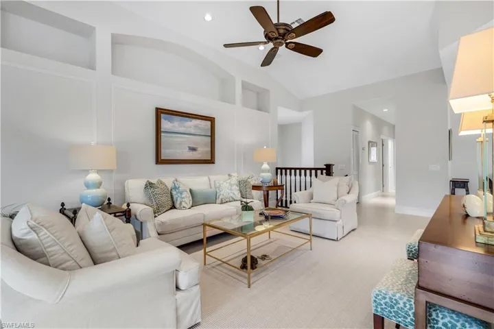 Living area featuring a ceiling fan, built in shelves, and vaulted ceiling