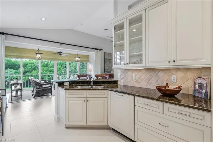 Kitchen featuring vaulted ceiling, dark stone countertops, glass insert cabinets, decorative backsplash, and light tile patterned floors