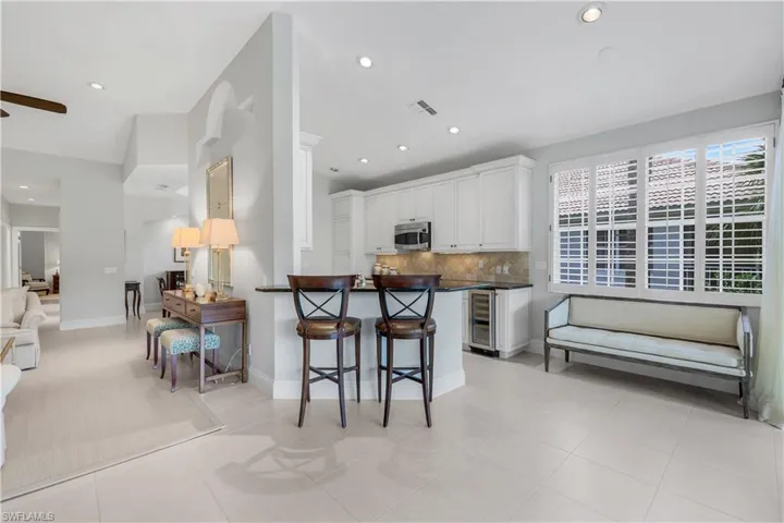 Kitchen featuring tasteful backsplash, a breakfast bar, white cabinetry, stainless steel microwave, and light tile patterned floors