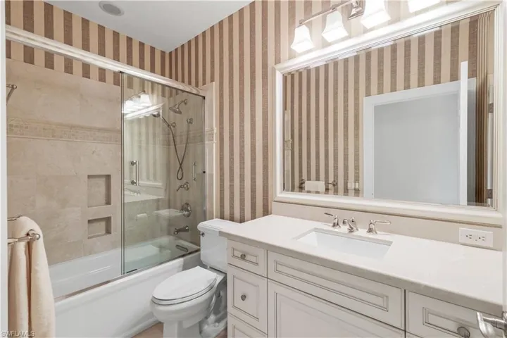 Full bathroom with shower / bath combination with glass door, wallpapered walls, and vanity