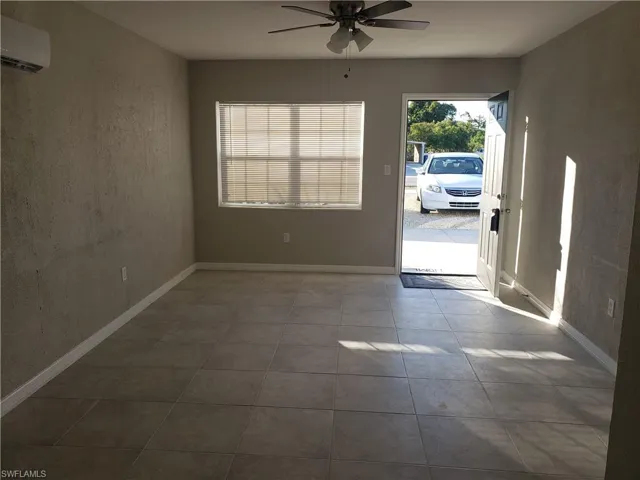 Unfurnished room featuring a ceiling fan, dark tile patterned flooring, a wall unit AC, and a textured wall