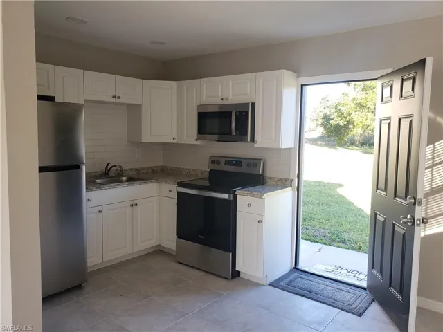 Kitchen featuring appliances with stainless steel finishes, decorative backsplash, white cabinets, and light tile patterned floors