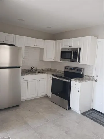 Kitchen featuring refrigerator, range, decorative backsplash, and white cabinetry