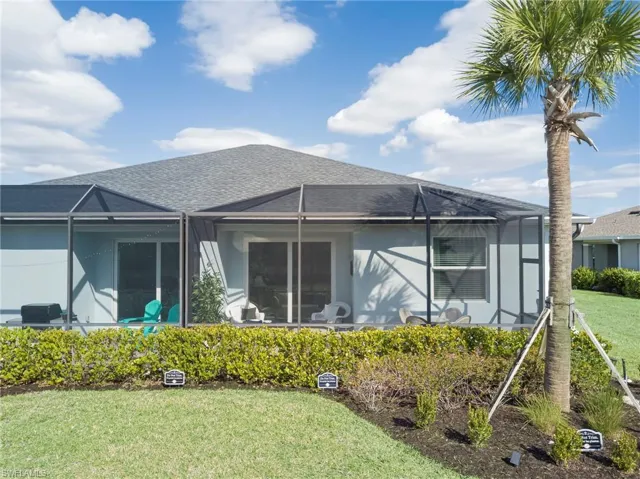 Rear view of house with a sunroom, glass enclosure, a shingled roof, a lawn, and stucco siding