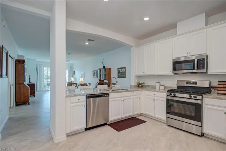 Kitchen featuring appliances with stainless steel finishes, white cabinetry, light stone counters, open floor plan, and recessed lighting