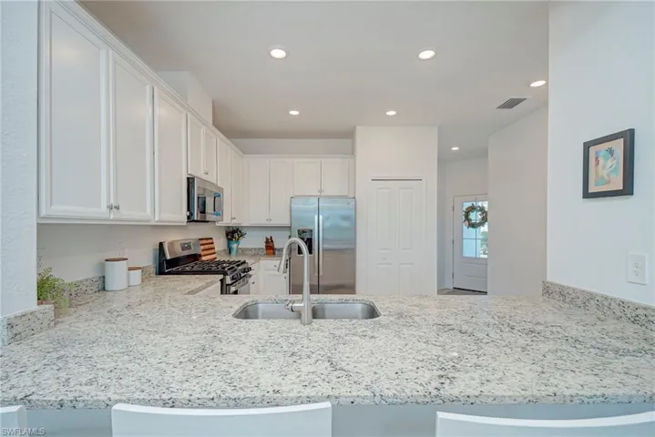 Kitchen featuring appliances with stainless steel finishes, white cabinets, light stone countertops, recessed lighting, and a peninsula