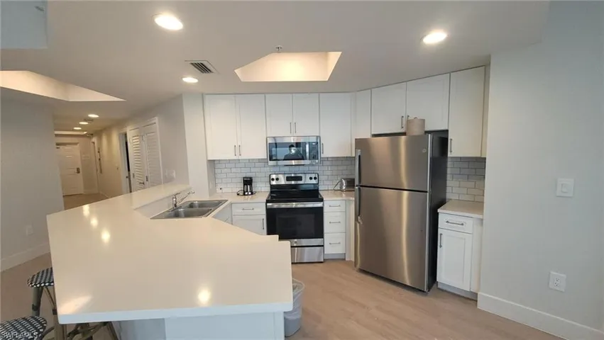 Kitchen with light countertops, a sink, appliances with stainless steel finishes, a peninsula, and visible vents