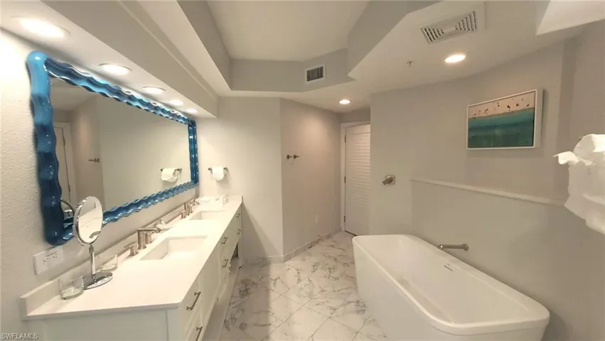 Bathroom featuring marble finish floor, visible vents, a soaking tub, and a sink