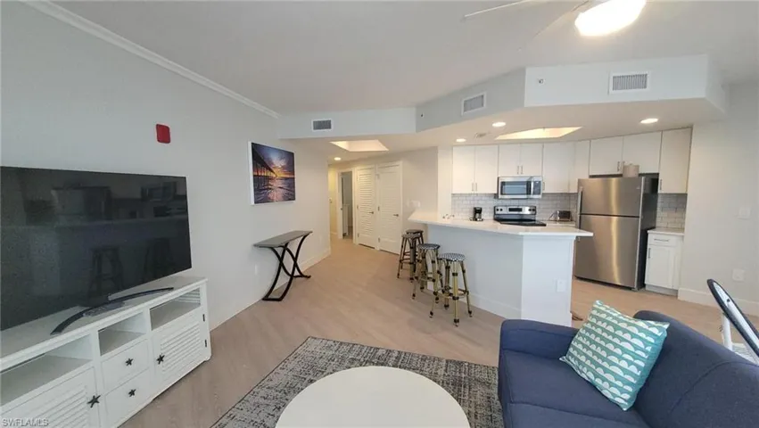 Living area featuring baseboards, visible vents, crown molding, and light wood-type flooring