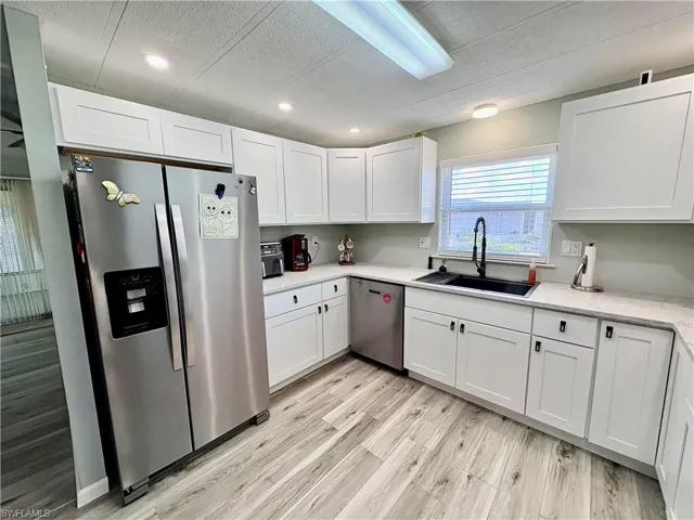 Kitchen with stainless steel appliances, white cabinets, light wood finished floors, light stone counters, and a textured ceiling