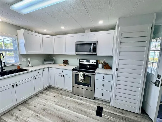 Kitchen featuring stainless steel appliances, white cabinetry, a textured ceiling, light wood-style floors, and light stone counters