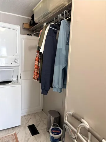 Laundry area featuring stacked washer and dryer and light marble finish floors