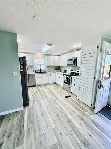 Kitchen featuring stainless steel appliances, white cabinetry, light countertops, light wood finished floors, and a textured ceiling