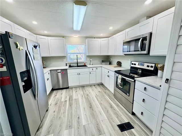 Kitchen with stainless steel appliances, white cabinetry, light wood-style flooring, recessed lighting, and a textured ceiling