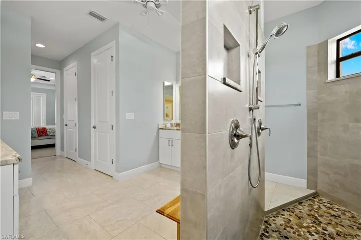 Bathroom with tiled shower, vanity, tile patterned floors, and ceiling fan