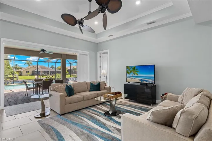 Living room with ornamental molding, light tile patterned flooring, ceiling fan, and a raised ceiling