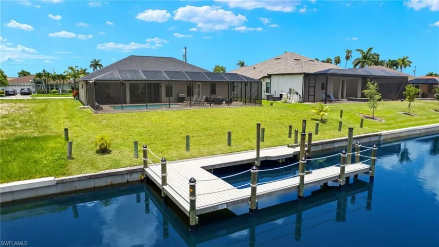 View of dock with a water view, a lanai, and a lawn