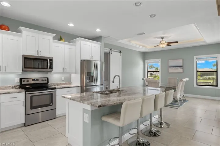 Kitchen with a tray ceiling, a kitchen island with sink, ceiling fan, and stainless steel appliances
