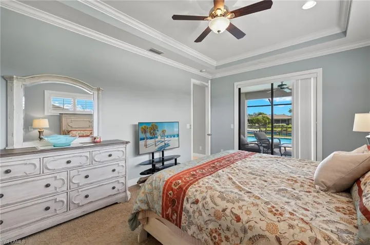 Carpeted bedroom featuring crown molding, ceiling fan, access to exterior, and a tray ceiling