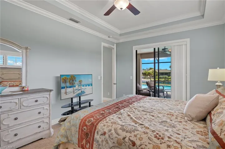 Carpeted bedroom featuring a tray ceiling, access to outside, multiple windows, and ceiling fan