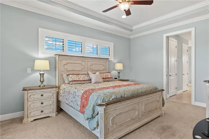 Bedroom with a raised ceiling, light colored carpet, crown molding, and ceiling fan