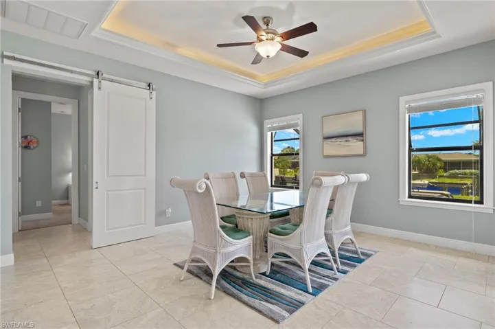 Tiled dining room with ceiling fan, a raised ceiling, and a barn door