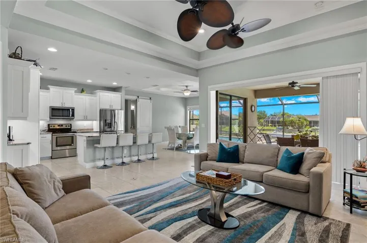 Living room featuring plenty of natural light, a tray ceiling, light tile patterned floors, and ceiling fan