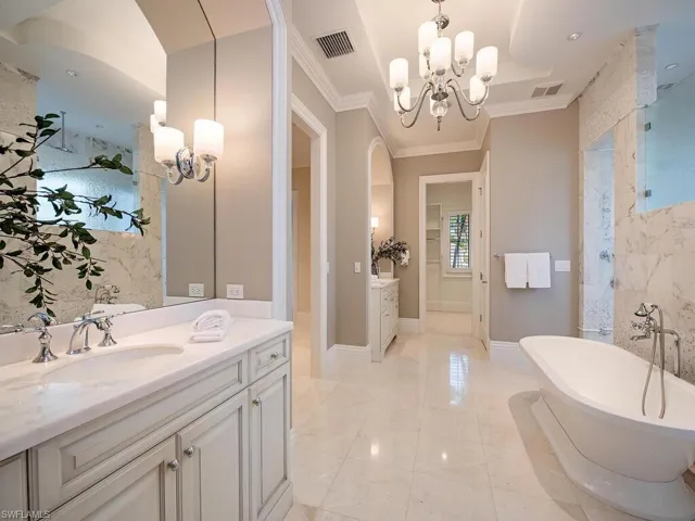 Bathroom with a chandelier, vanity, crown molding, and a tub