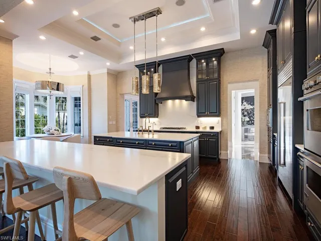 Kitchen featuring hanging light fixtures, dark hardwood / wood-style floors, an island with sink, a tray ceiling, and custom range hood