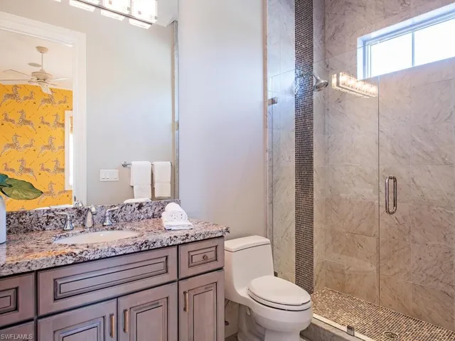 Bathroom featuring ceiling fan, a shower with door, vanity, and toilet